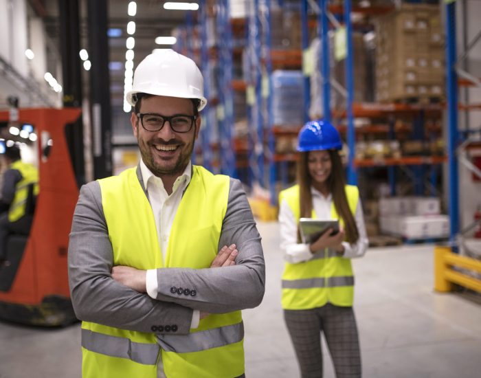 portrait of successful warehouse worker or supervisor with crossed arms standing in large storage distribution area.